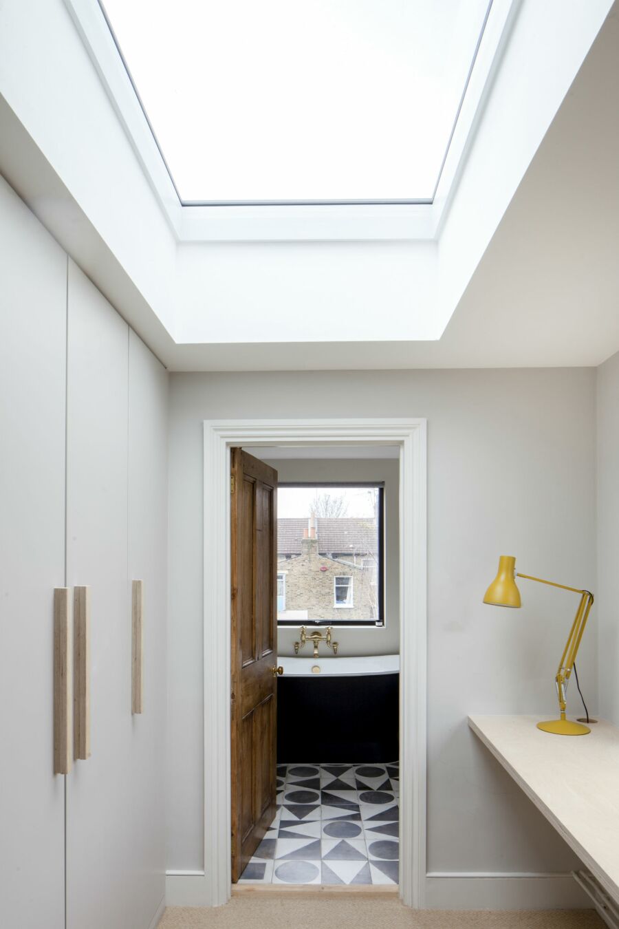 Room with skylight that looks through to a bathroom with a roll-top bathtub with brass taps.